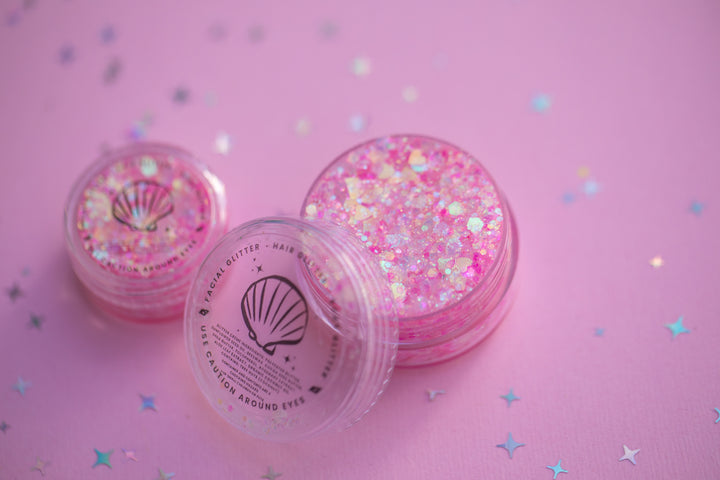 Pink glitter containers on a pink background with star patterns