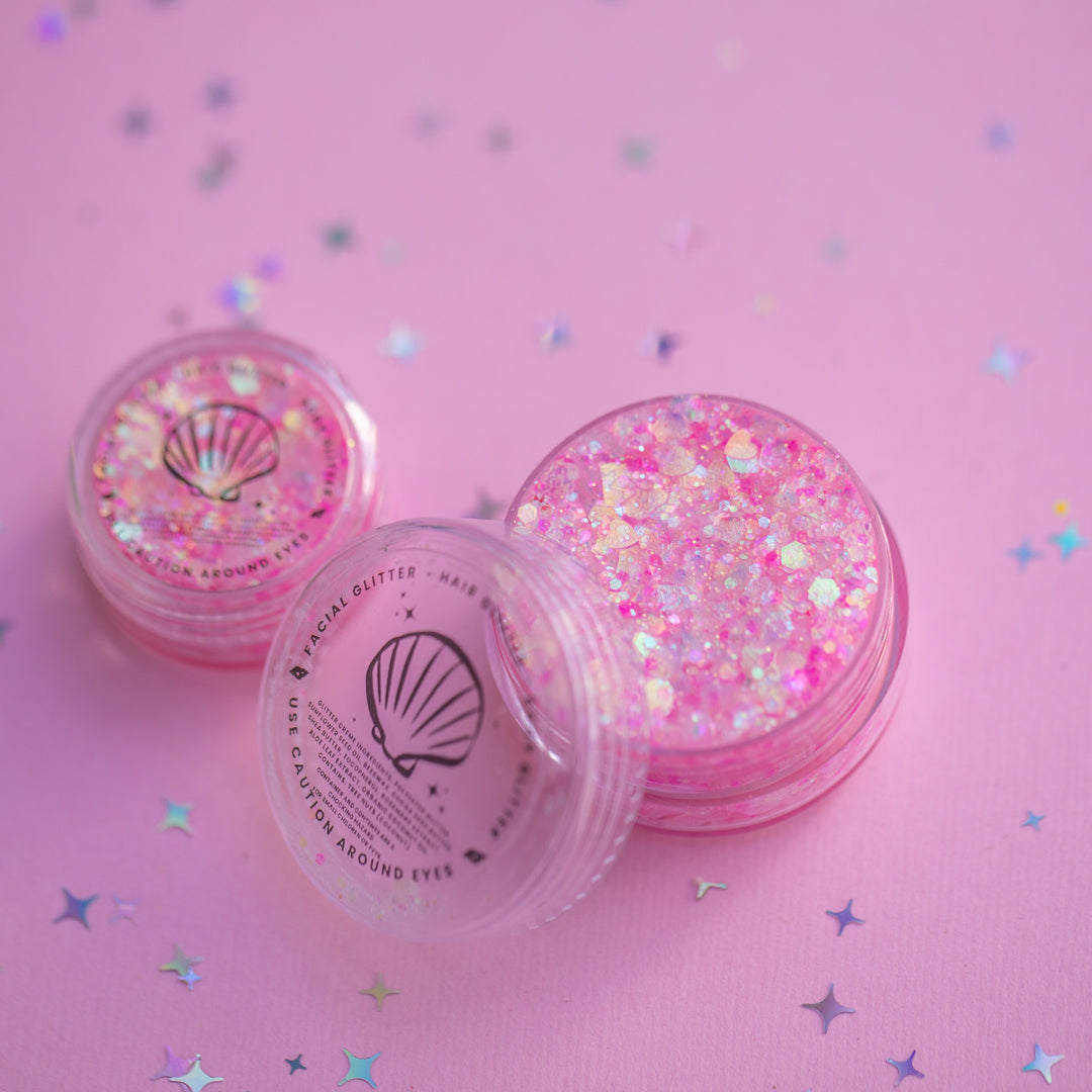 Two containers of pink glitter with a shell design on a pink background with star confetti.