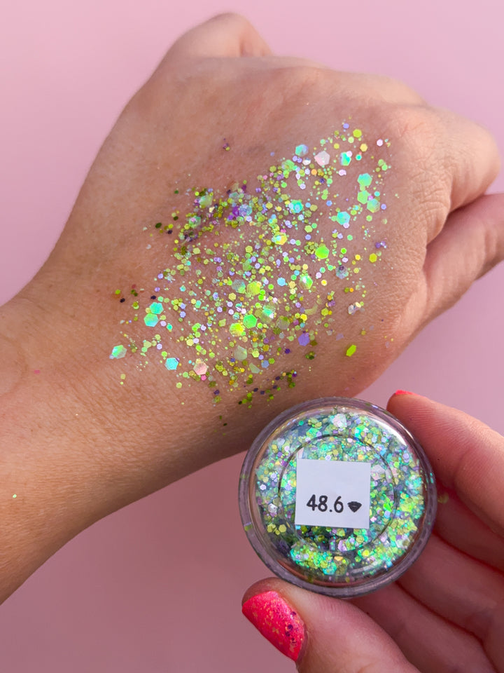 Hand with glitter on skin and container of glitter against a pink background