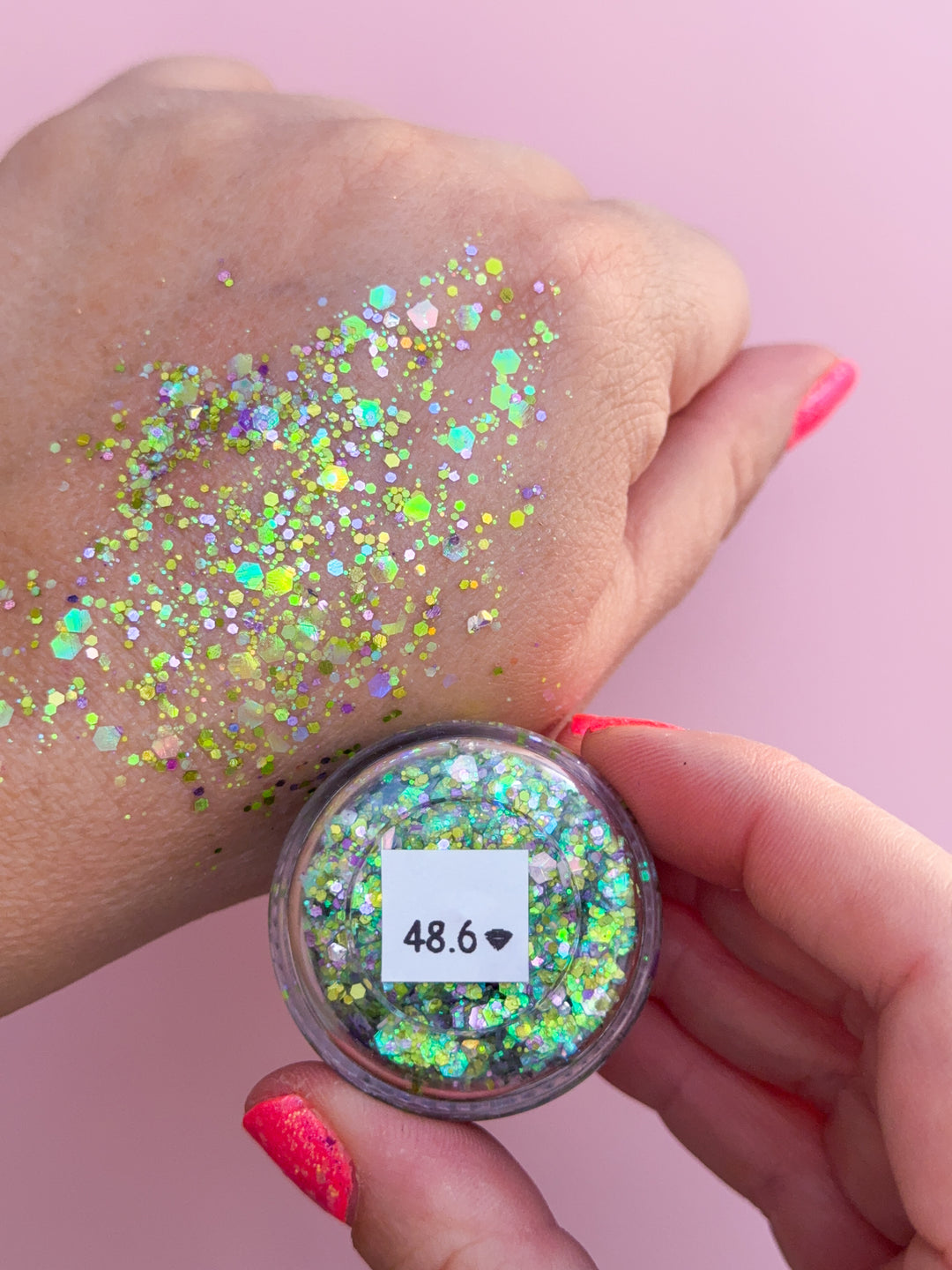 Hand applying glitter to skin with a container of glitter on a pink background