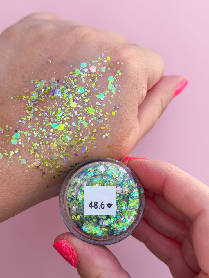 Hand applying glitter to skin with a container of glitter on a pink background