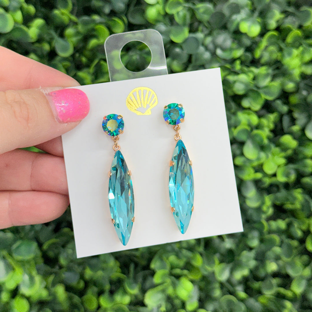 Turquoise earrings on a card held against a green foliage background