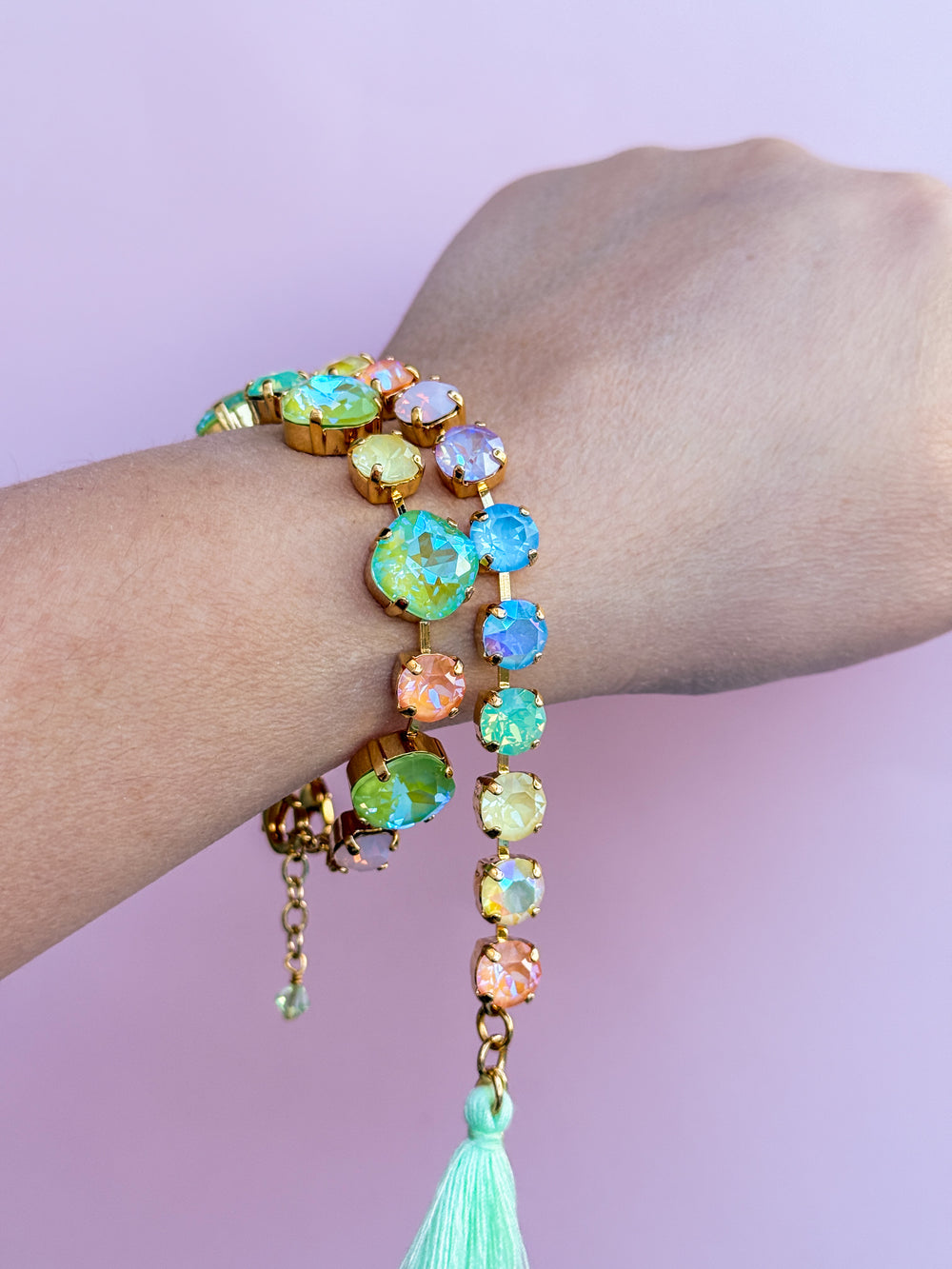 Multicolored beaded bracelet with a tassel on a wrist against a light purple background