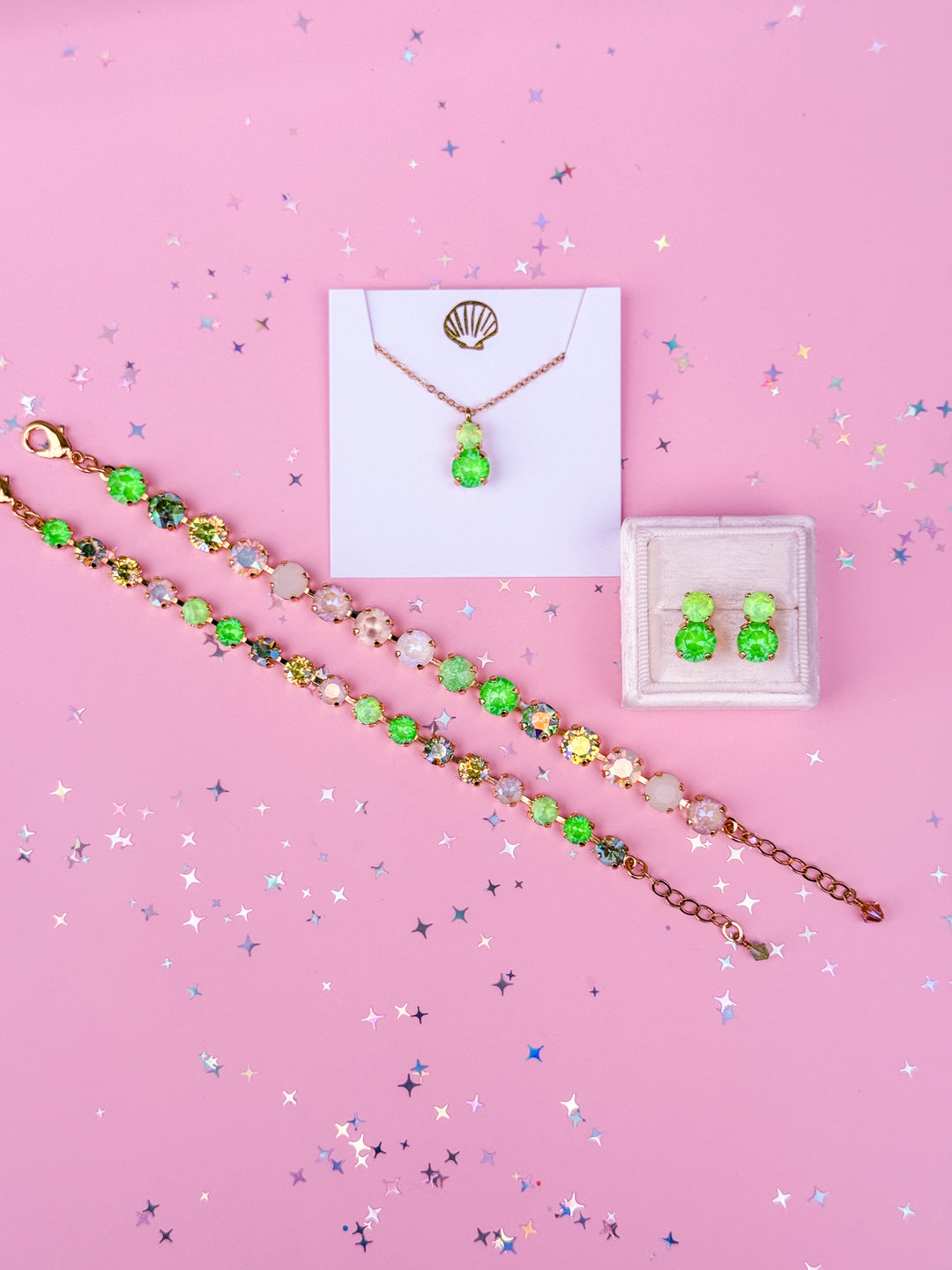 Jewelry set including a necklace, bracelet, and earrings on a pink background with confetti.