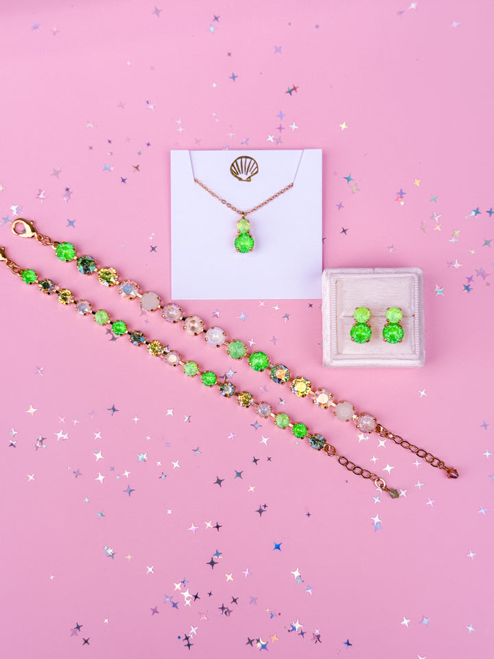 Jewelry set including a necklace, bracelet, and earrings on a pink background with confetti.