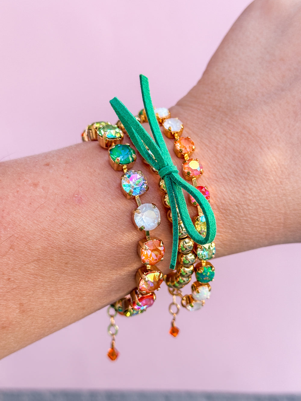 Colorful beaded bracelet with a green cord on a wrist against a pink background