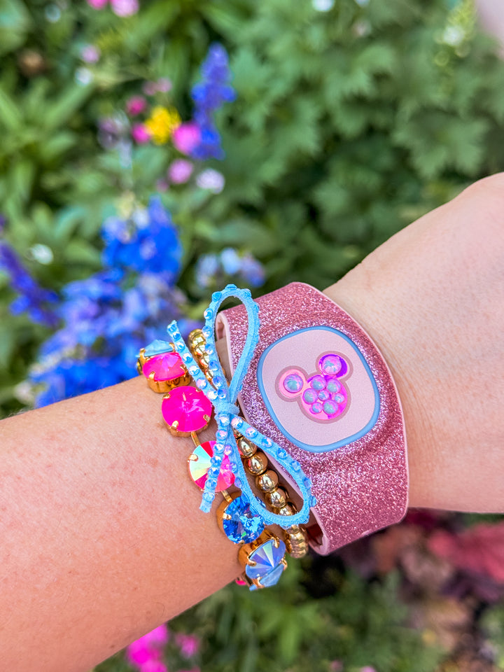 Pink glittery wristband with a character design worn on a wrist against a blurred natural background