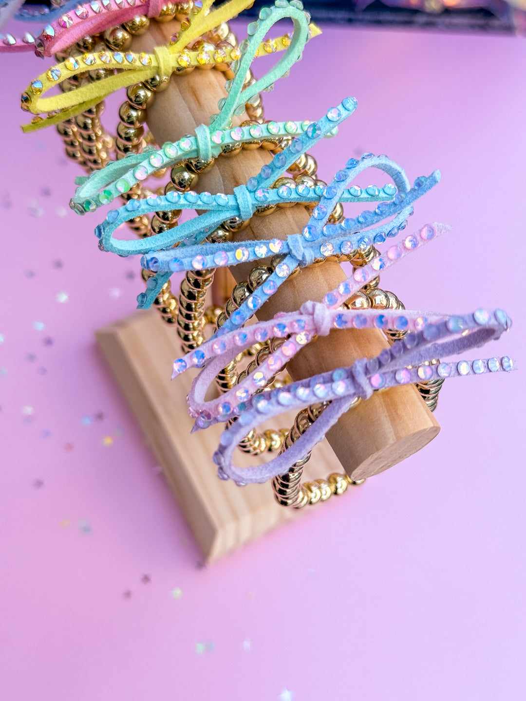 Colorful bracelets with rhinestones on a wooden block against a pink background