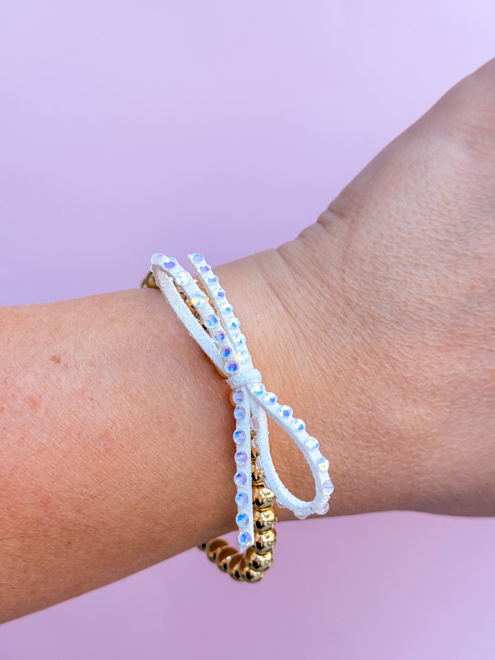 Close-up of a wrist wearing two beaded bracelets against a light purple background