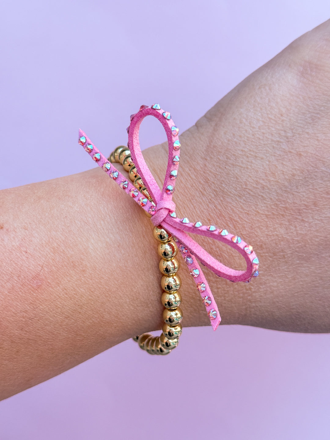 Pink beaded bracelet with gold beads on a wrist against a purple background