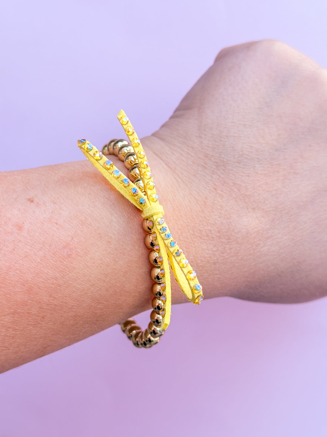 Yellow beaded bracelet on a wrist with a light purple background
