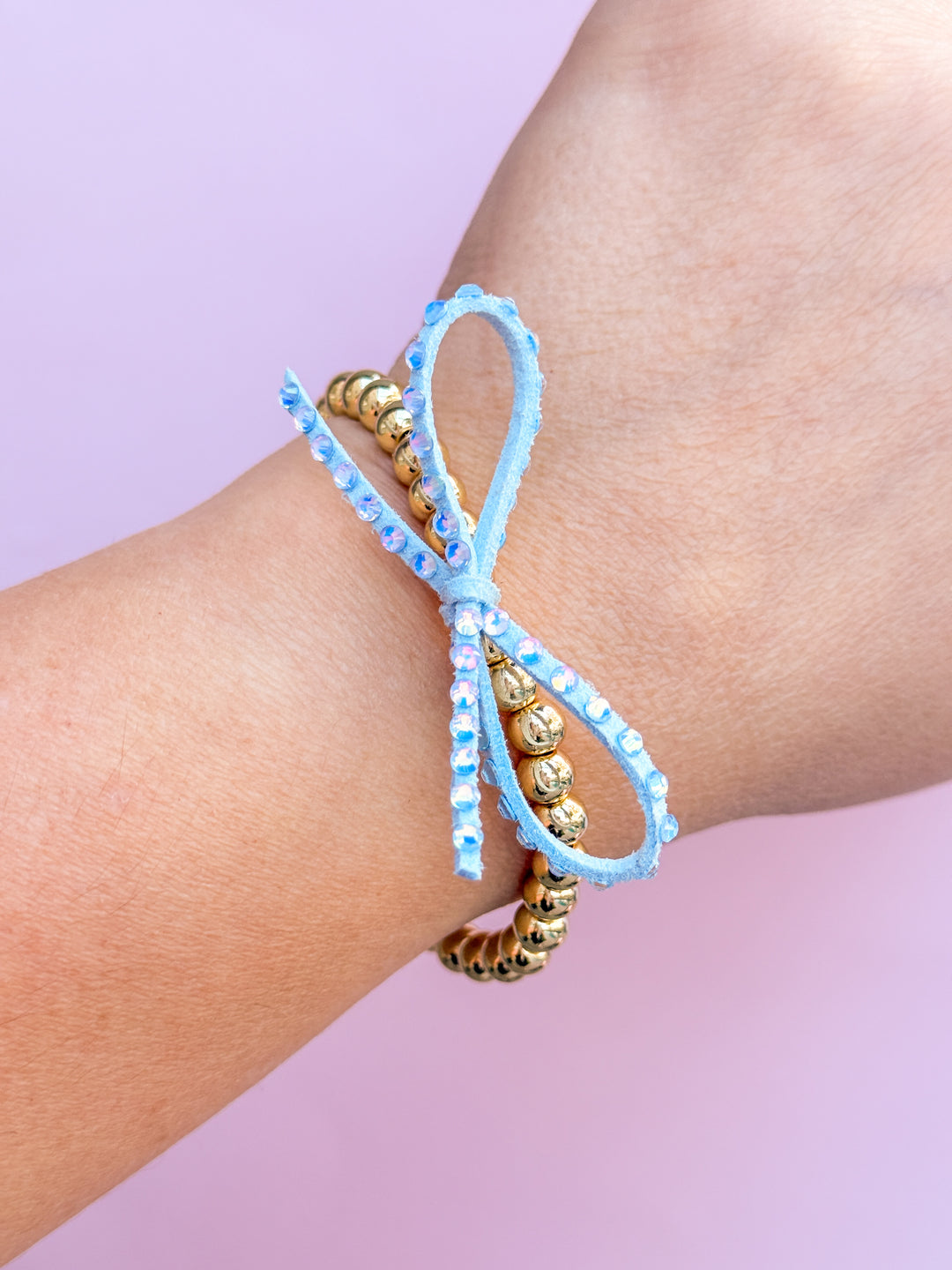 Light blue beaded bracelet with gold accents on a wrist against a pink background