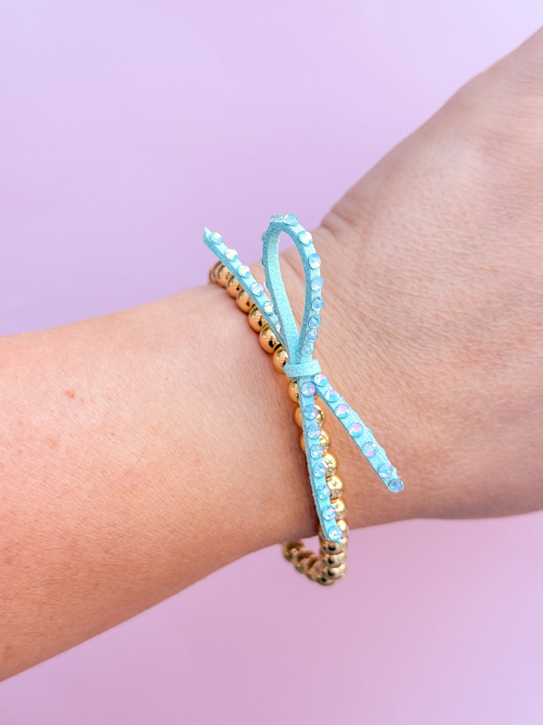 Mint blue beaded bracelets on a wrist against a light purple background