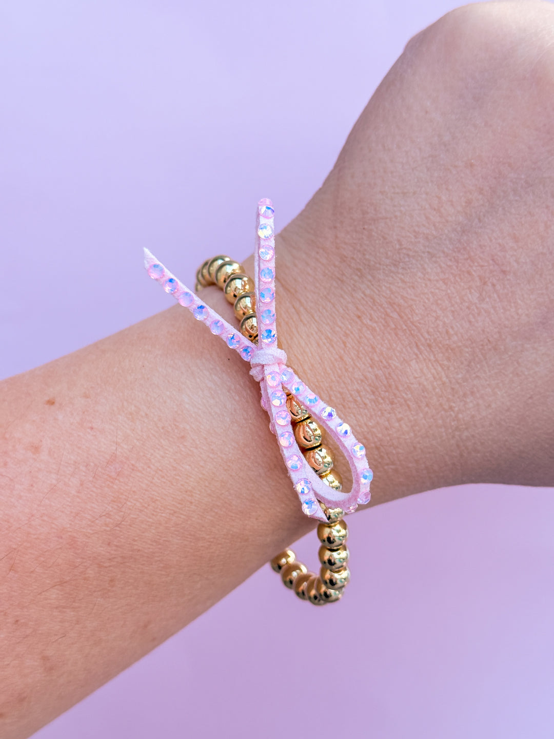 Bracelet with pink beads and gold accents on a wrist against a purple background