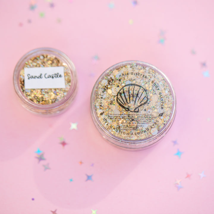 Two containers of glitter with 'Sand Castle' and 'Seashell' labels on a pink background.