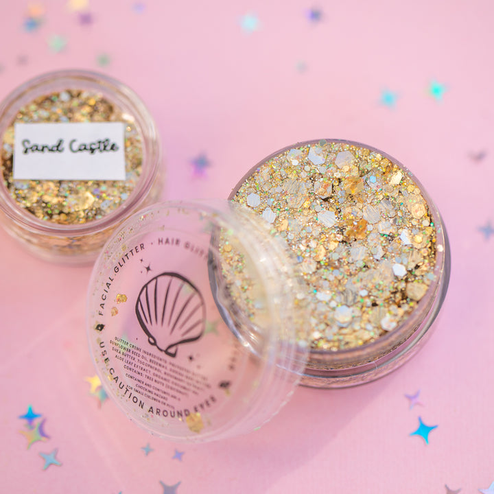 Two containers of glitter on a pink background with star-shaped confetti.