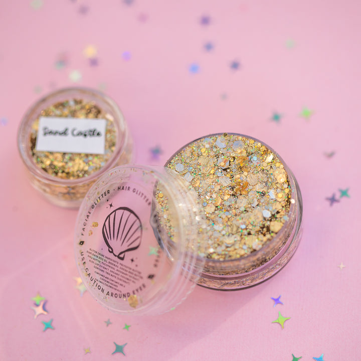 Two containers of glitter on a pink background with star-shaped confetti.