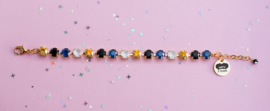 Bracelet with colorful gemstones and a heart-shaped tag on a pink background