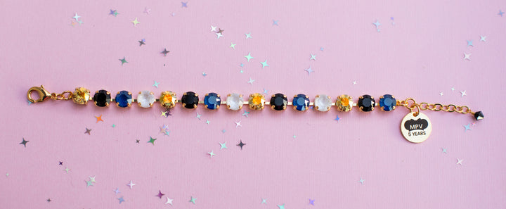 Bracelet with colorful gemstones and a heart-shaped tag on a pink background