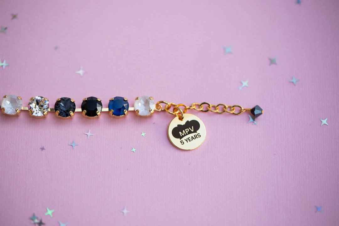 Bracelet with gemstones and a gold tag on a pink background