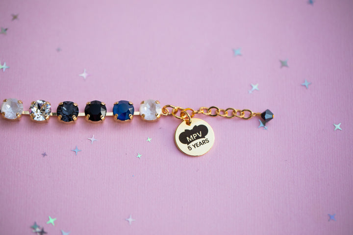 Bracelet with gemstones and a gold tag on a pink background