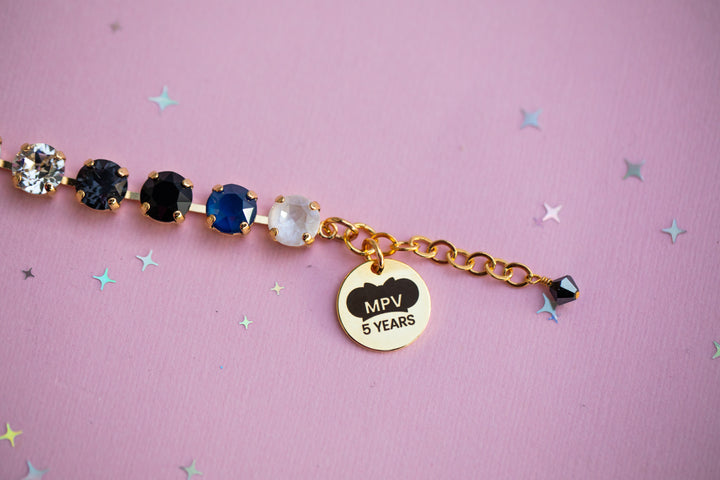 Bracelet with gemstones and 'MPV 5 YEARS' charm on a pink background