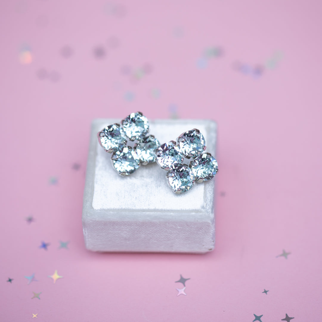 Pair of clover shaped earrings on a white box with a pink background