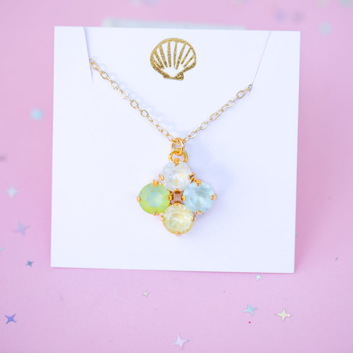 Gold necklace with pastel-colored gemstones on a white card with a gold shell design, against a pink background.