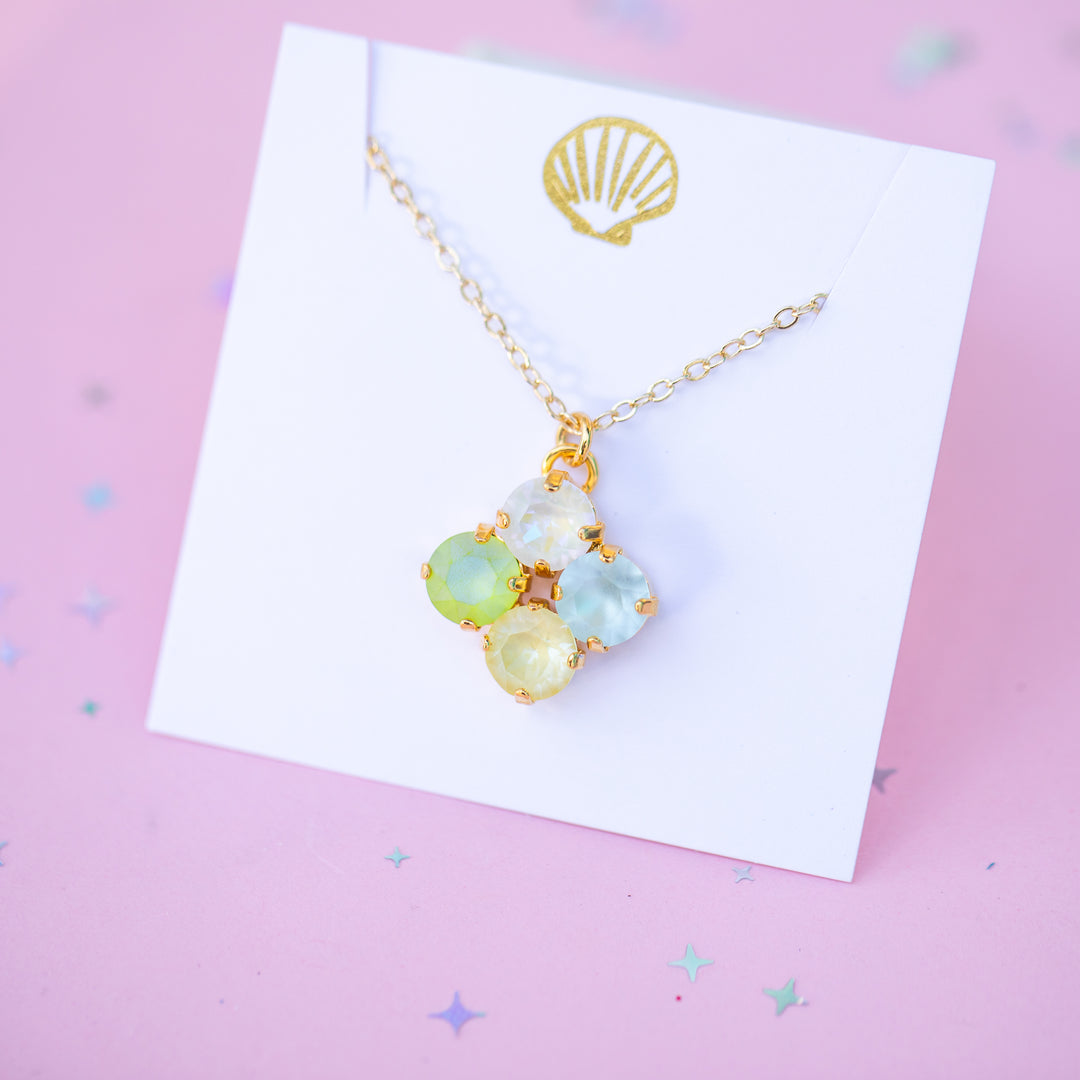 Necklace with colorful pendant on a white card with a gold shell design, against a pink background.
