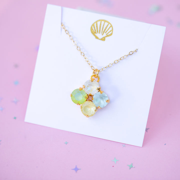 Necklace with colorful pendant on a white card with a gold shell design, against a pink background.