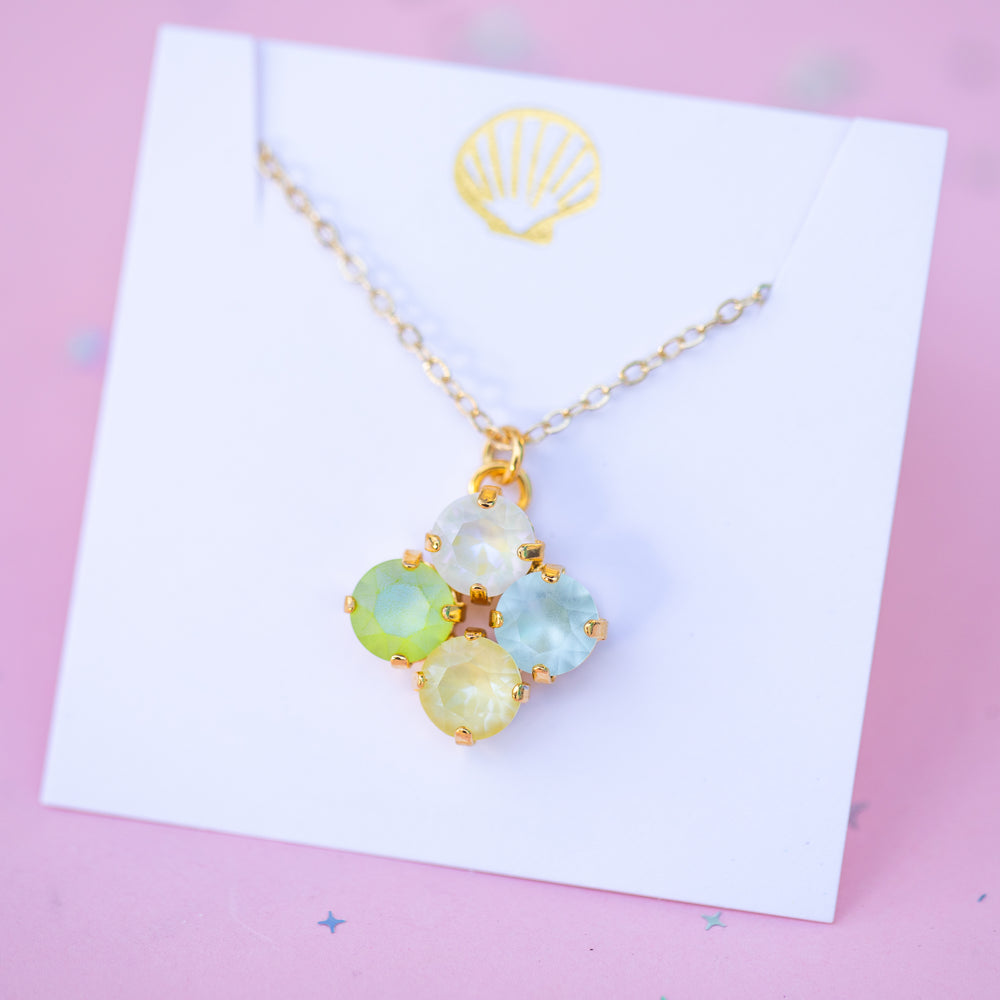 Necklace with colorful pendant on a white card with a gold shell design, against a pink background.