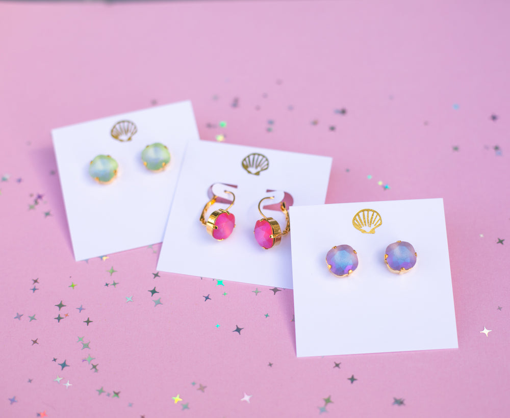 Colorful earrings on white cards against a pink background with confetti