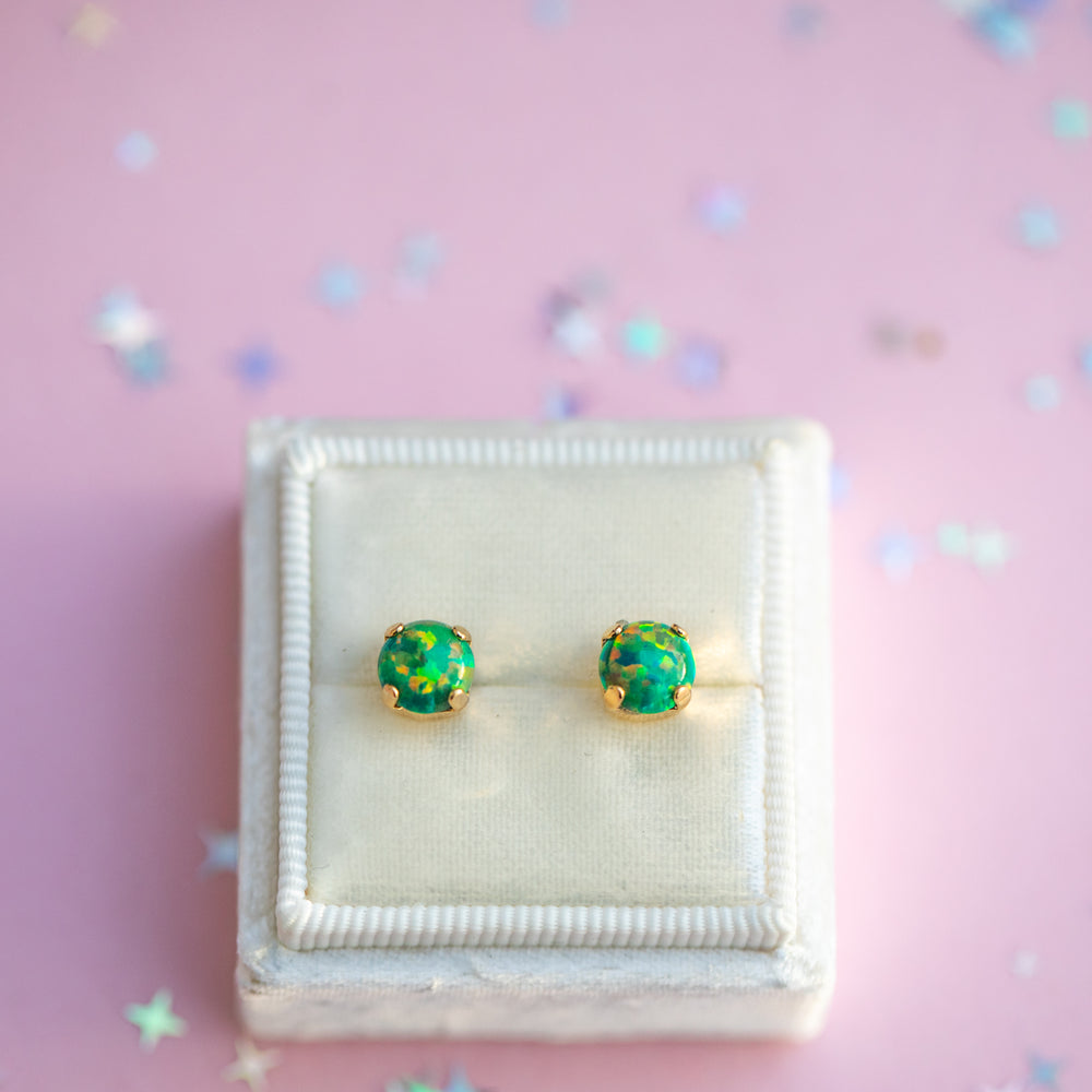 Green opal stud earrings in a jewelry box on a pink background with star-shaped confetti.