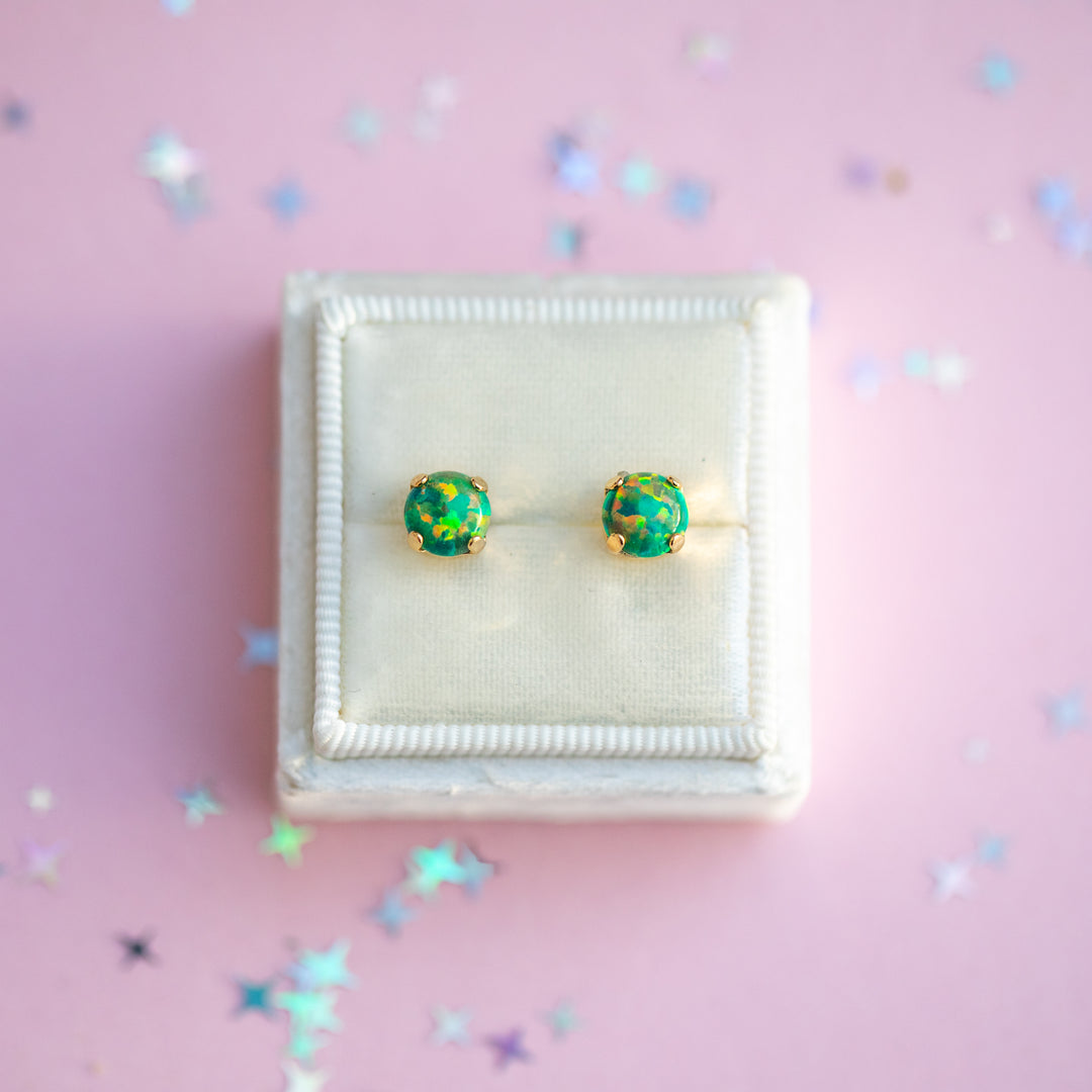 Green earrings in a white box on a pink background with star-shaped confetti.