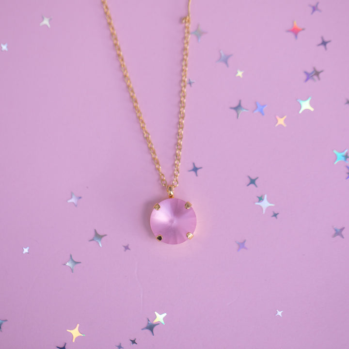 Necklace with a pink pendant on a pink background with star-shaped confetti