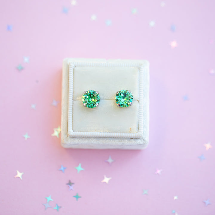 Green gemstone earrings in a white box on a pink background with star-shaped confetti.