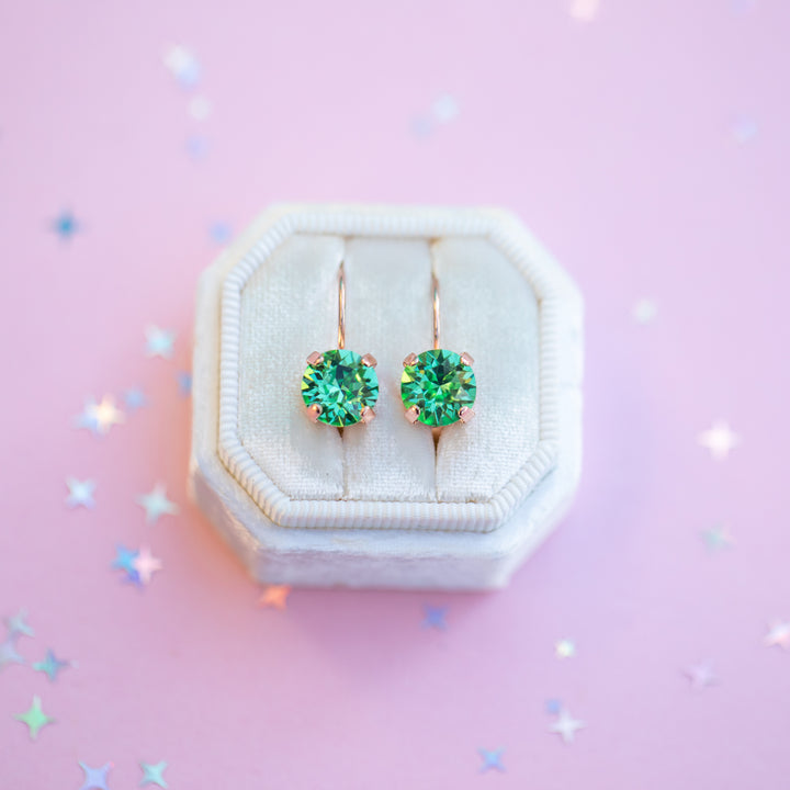 Green gemstone earrings in a white jewelry box on a pink background