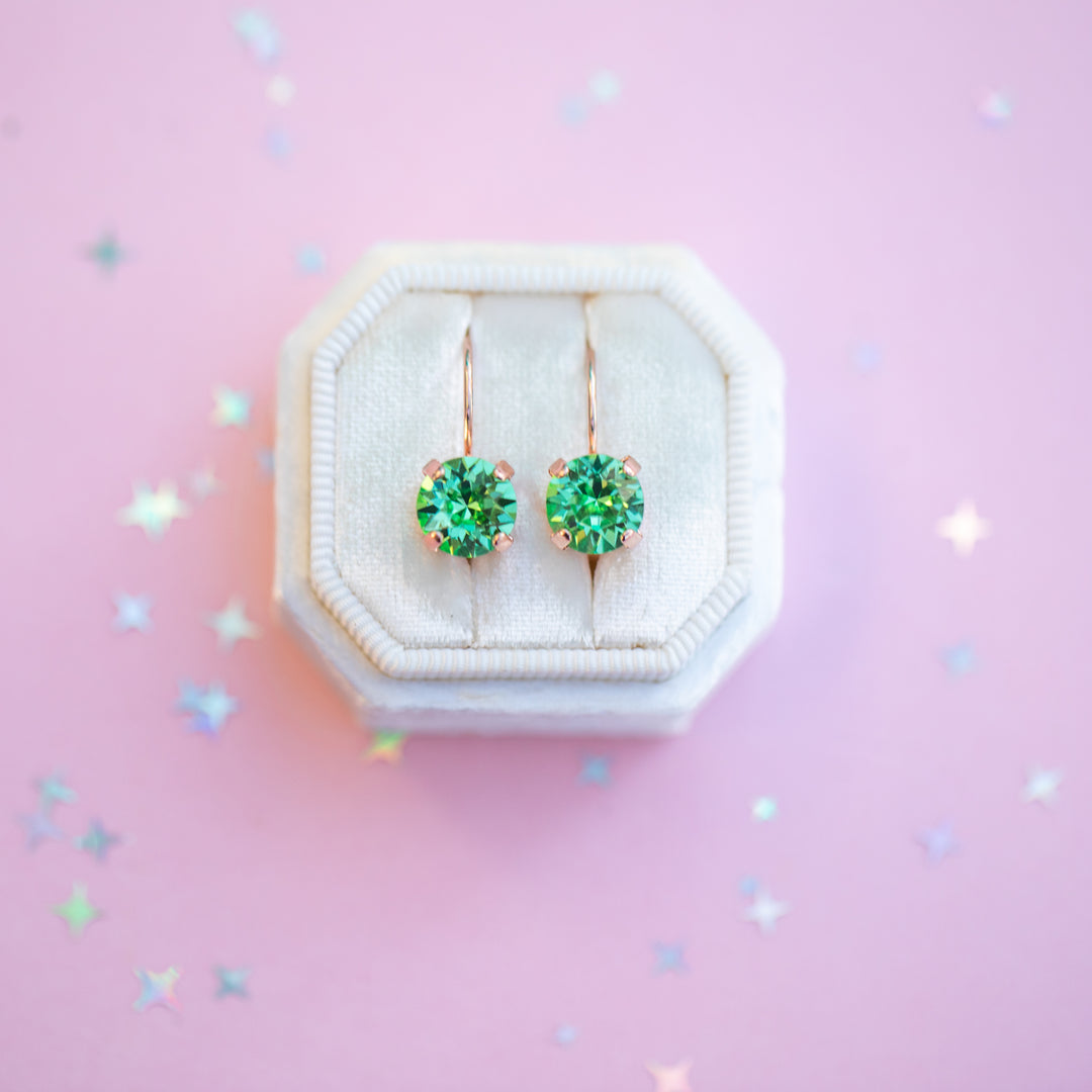Green gemstone earrings in a white jewelry box on a pink background