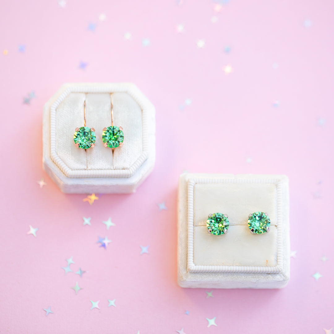 Green gemstone earrings in a white jewelry box on a pink background