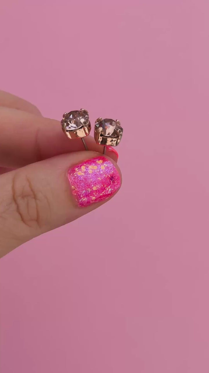 A pair of round-cut rose gold stud earrings with sparkling peach gemstones held in fingers
