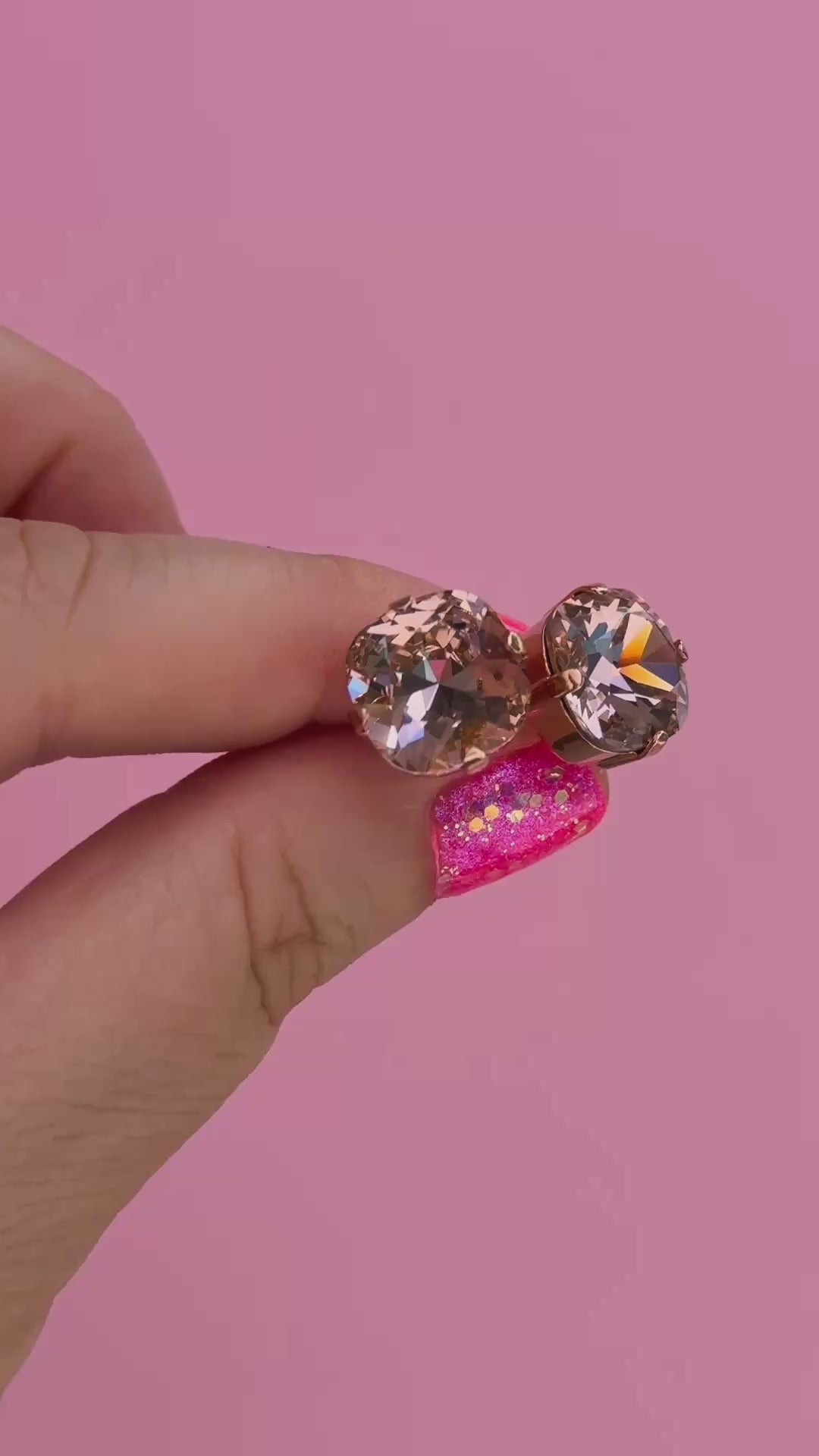 A pair of rose gold stud earrings with cushion cut faceted warm toned pink gemstone crystals in a hand showing them for size.