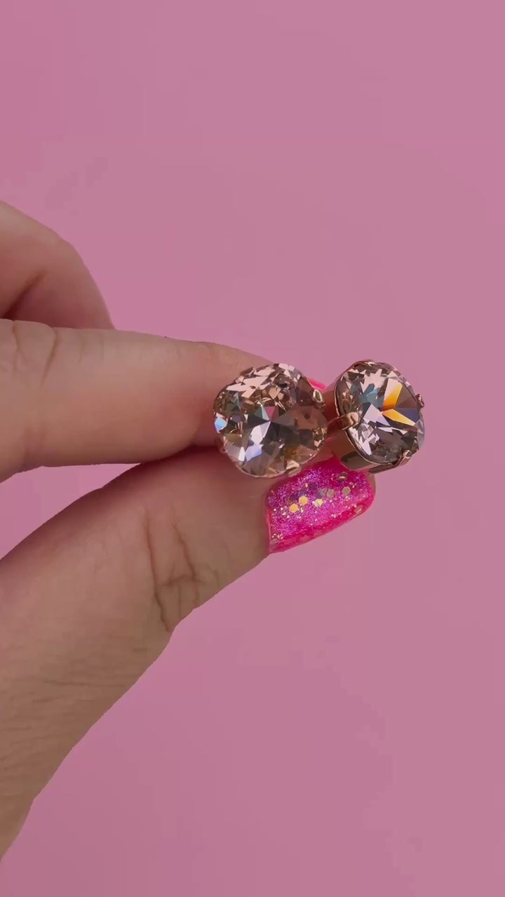A pair of rose gold stud earrings with cushion cut faceted warm toned pink gemstone crystals in a hand showing them for size.