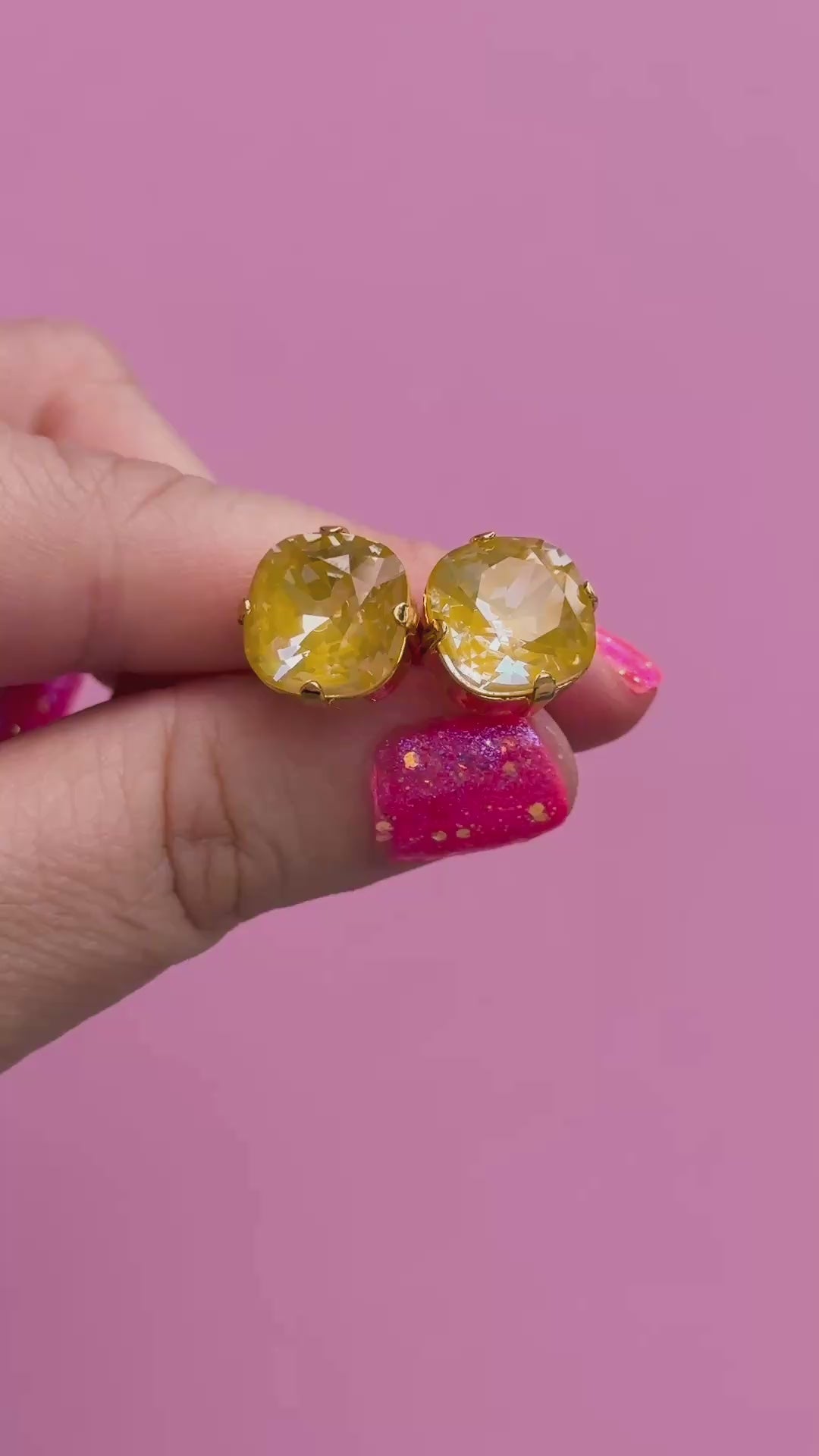 A pair of mustard yellow faceted cushion cut stud earrings held in a hand to show the size