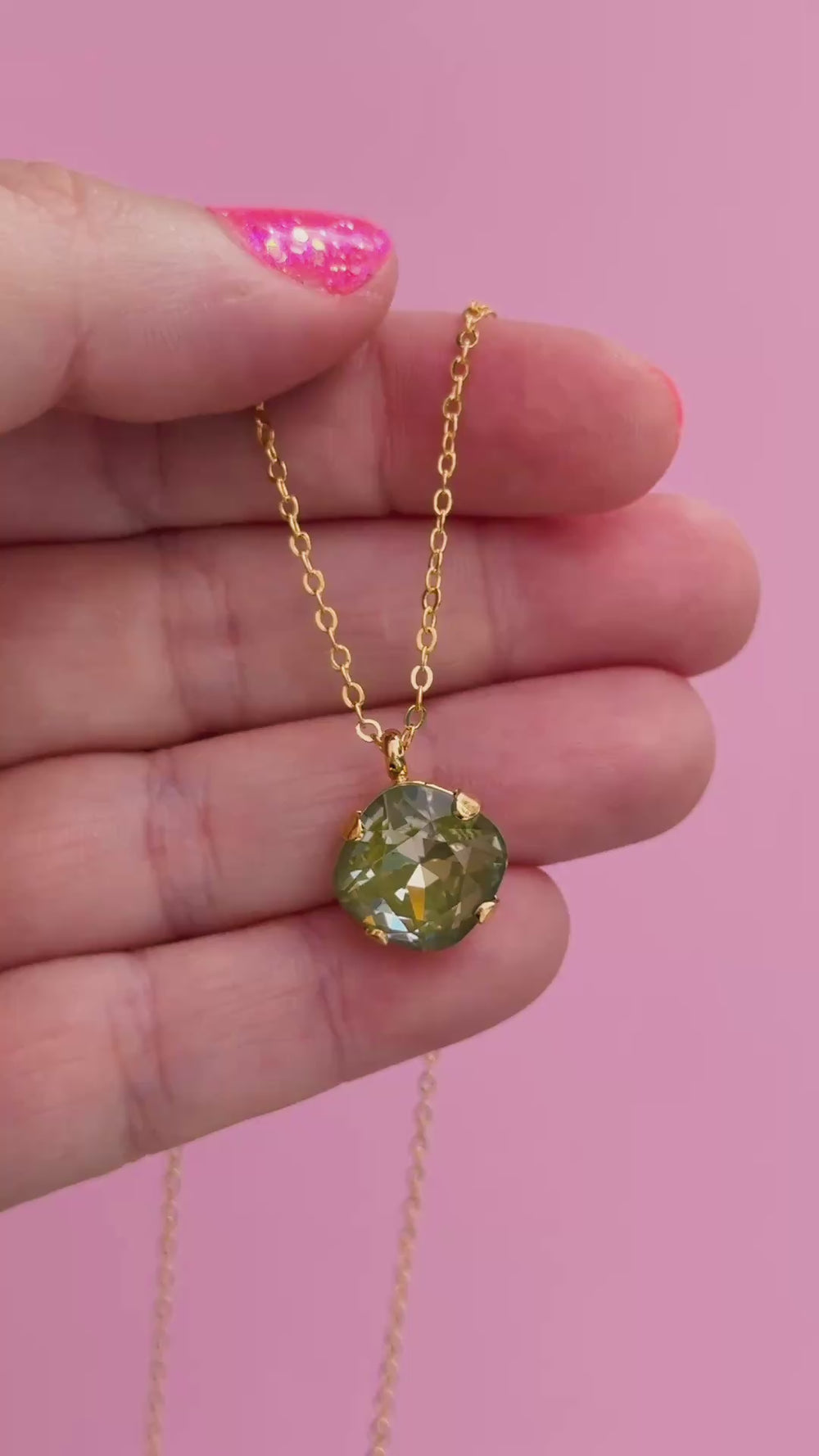 A gold chain necklace with a faceted cushion cut olive green crystal pendant, shown on a hand.