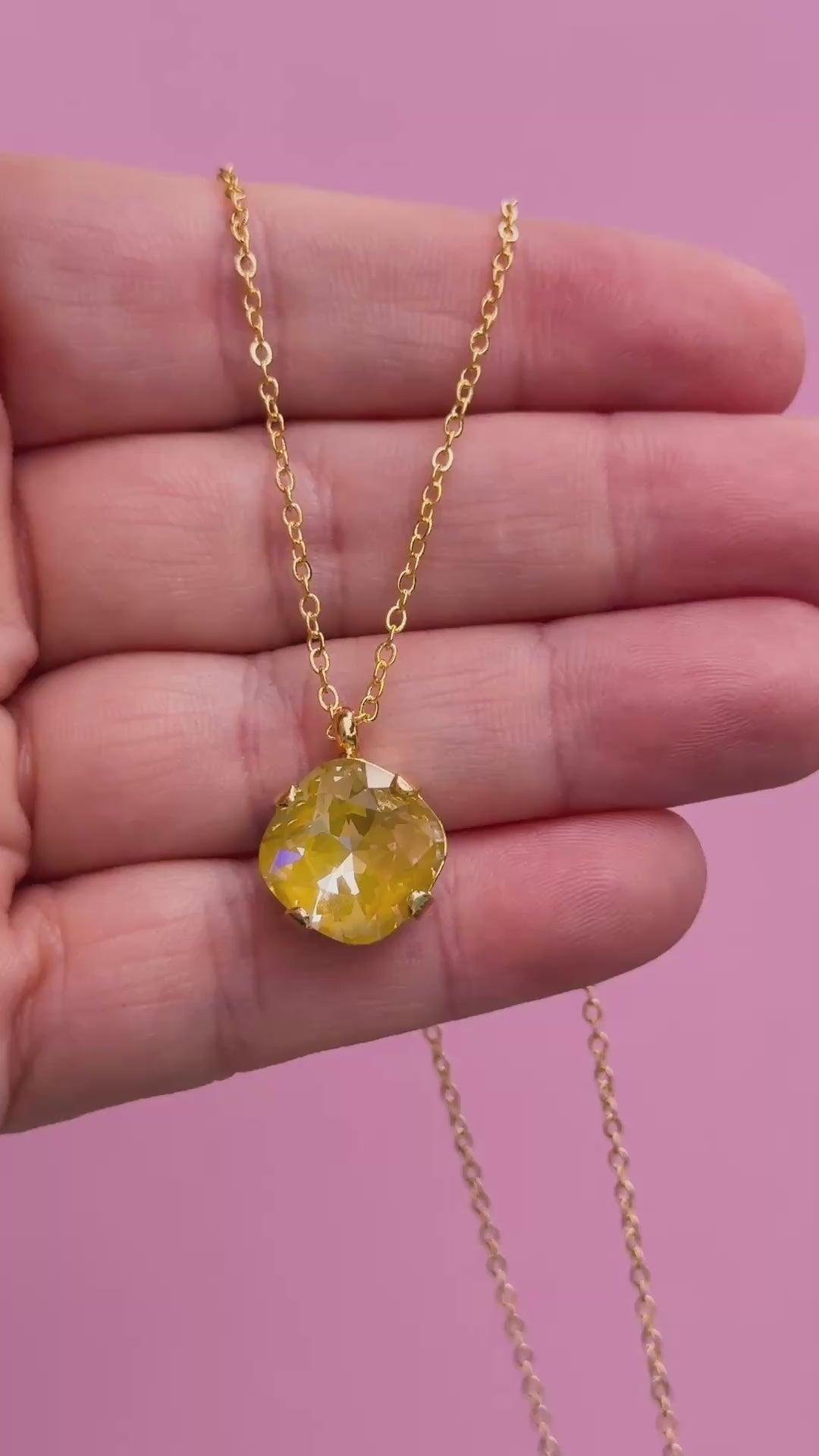 A gold chain necklace with a cushion cut faceted yellow crystal pendant held in a hand.