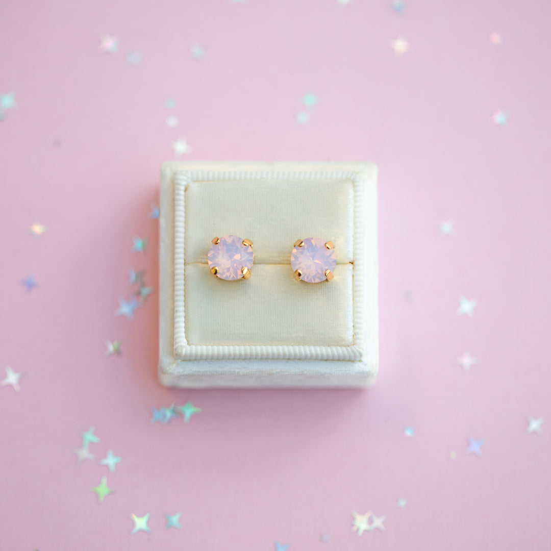 Pair of pink earrings in a white jewelry box on a pink background with star-shaped decorations.
