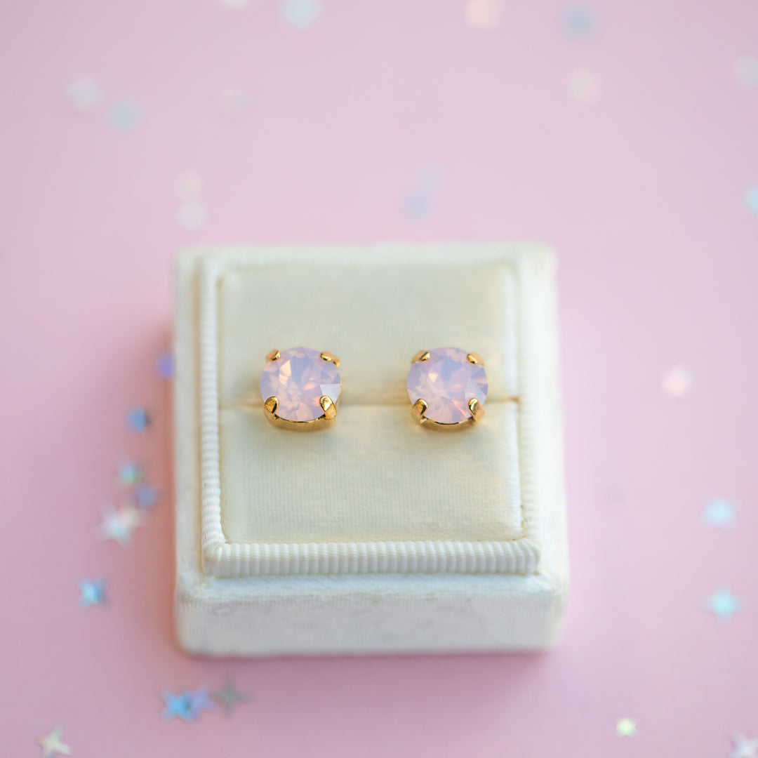 Pair of pink opal stud earrings in a white jewelry box on a pink background with star-shaped confetti.