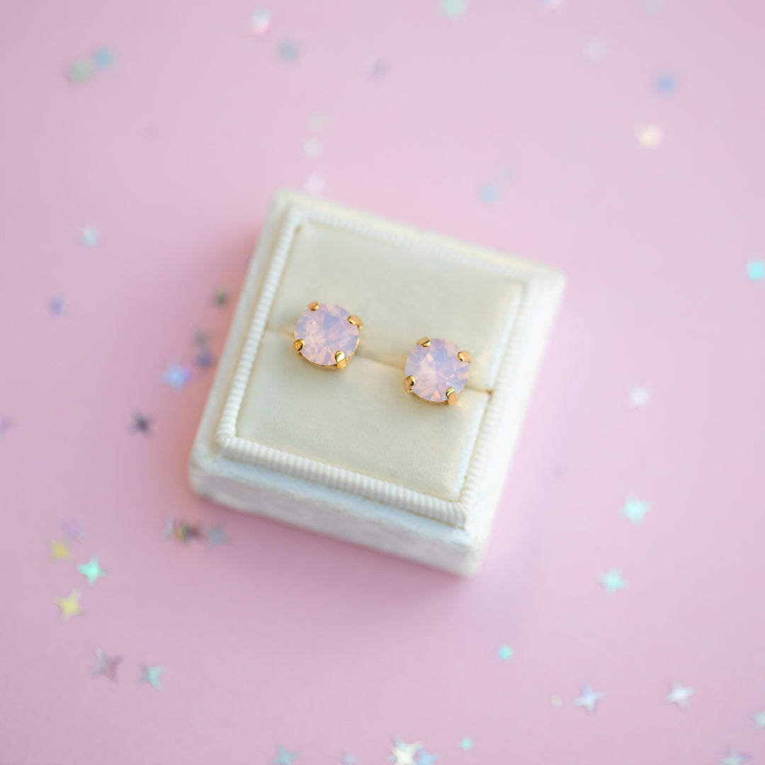 Pair of gold earrings with pink gemstones on a pink background