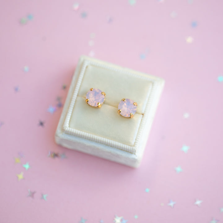 Pair of gold earrings with pink gemstones on a pink background