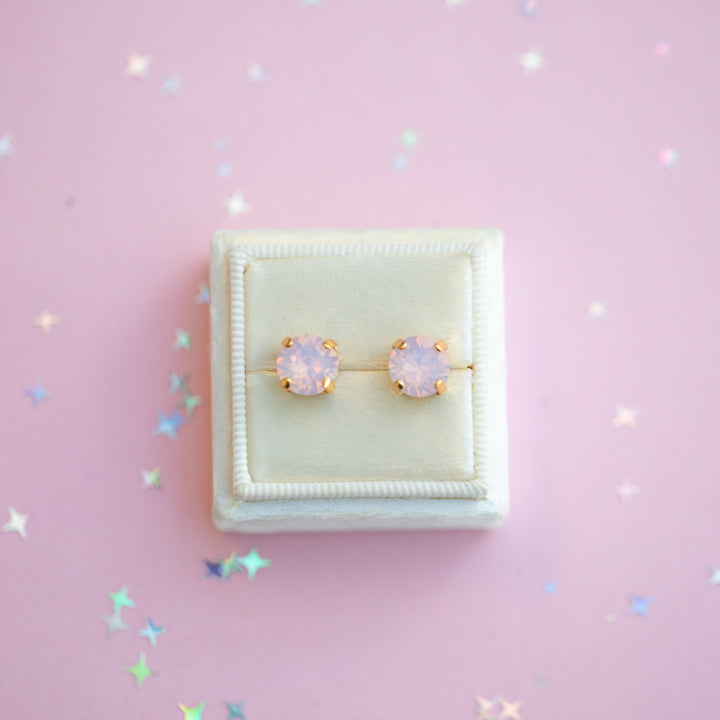 Pair of pink opal earrings in a white box on a pink background with star-shaped confetti.
